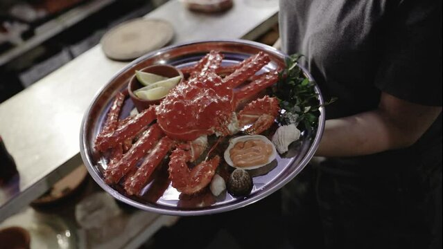 Seafood and gastronomy. Top view of a waitress holding a tray with a fresh King Crab dish in the kitchen.