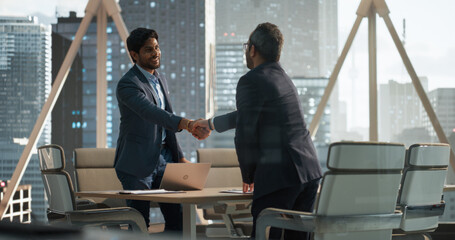 South Asians Business Partners Striking a Successful Deal at a Corporate Modern Meeting Room. Two Young Indian Businessmen Shaking Hands After a Positive Negotiation Process - obrazy, fototapety, plakaty