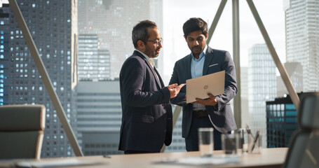 Two Young South Asian Businessmen Standing Next to a Window in a Modern Office with a City Skyline...