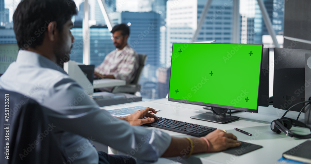 Poster Indian Chief Financial Officer Working on Desktop Computer with Green Screen Mock Up Display. Young South Asian Specialist Analyzing Corporate Banking Account, Researching Investment Opportunities