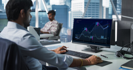 Hedge Fund Office: Indian Financial Analyst Using Computer with Display Showing Real-Time Stocks, Exchange Market Charts. Hard Working South Asian Trader Making Profitable Investment.