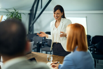 A smiling businesswoman talking to her colleagues, standing during the meeting.