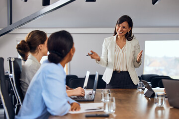A smiling businesswoman talking to her colleagues in the meeting room. - 753135850