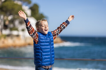 Smiling boy with arms outstretched on a beach.
