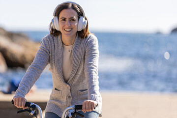 Woman riding a bicycle by the sea, listening to music with headphones.