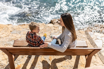 Young mother chatting with her son on a bench by the sea.