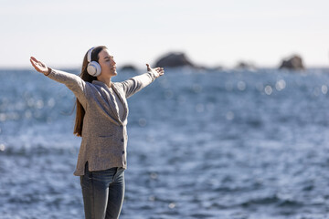 Young woman standing, listening to music with arms outstretched, and breathing fresh sea air