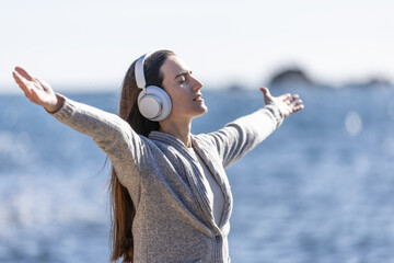 Young woman listening to music with arms outstretched, and breathing fresh sea air