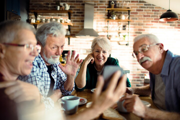 Group of happy seniors enjoying breakfast and using smartphone together