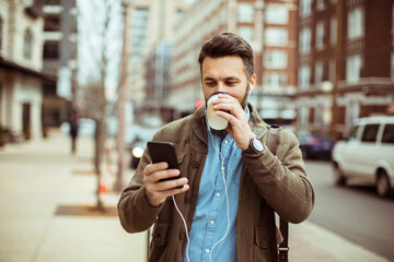Man drinking coffee and looking at smartphone in city