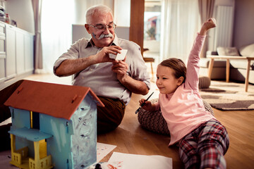 Grandfather and granddaughter painting a toy house together at home