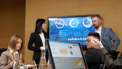 Beautiful business woman and man are giving a report to their business colleagues in the conference room, they are showing graphs, pie charts and company growth on the wall mounted TV.