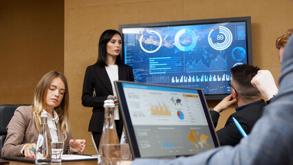 Business meeting in the conference room. A businesswoman is talking to her colleagues while an animated chart data is displayed on the computer screen.