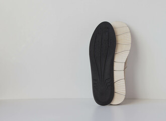 The black insole and sole of the sports shoe are positioned vertically. Light background. Foot care products conception.