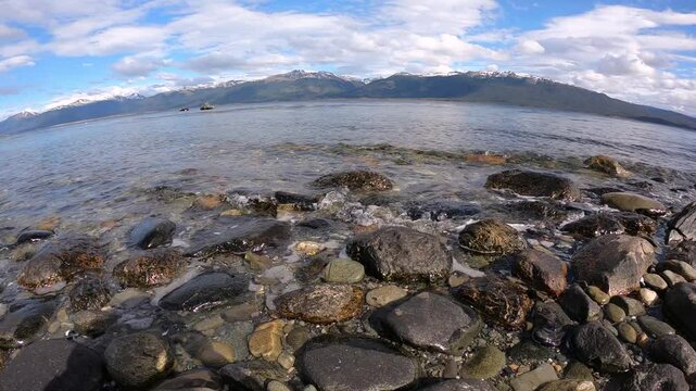 Panorama view of the calm ocean waves in the rocky shore. A couple of fishing boats and the Andes mountains in the horizon. 