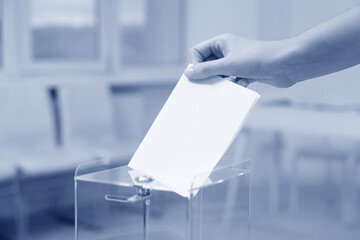 Woman putting her vote into ballot box indoors, closeup. Color toned