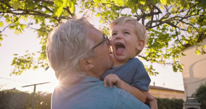 at sunset, in the garden, the grandfather plays with his little grandson.
The grandfather blows up the child and finally they laugh and hug each other