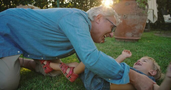 at sunset, in the garden, the grandfather tickles his little grandson and they laugh together