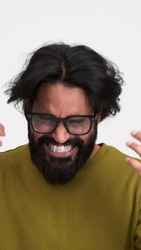 Excited young man with beard and eyeglasses screaming ecstatically and pumping fists while celebrating victory over white background