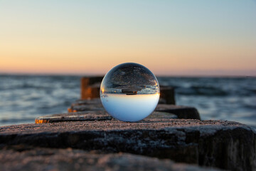 The beach and sea are reflected in a glass ball that lies on a wooden breakwater