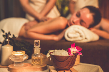 Obraz na płótnie Canvas Aromatherapy massage ambiance or spa salon composition setup with focus decor candles and spa accessories on blur couple enjoying blissful aroma spa massage in resort or hotel background. Quiescent