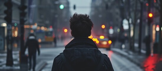 Man in black jacket walking alone on city street from behind in slow motion.