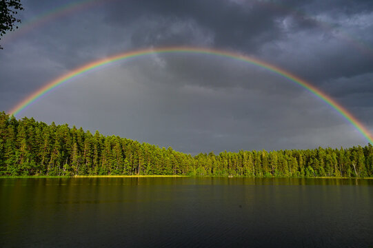 Double rainbow with main rainbow with interference arcs and secondary rainbows over Lake Helgasjön and trees in the background in Helgö National Park, Växjö, Kronobergs län, Smaland, Sweden