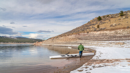 Senior male rower with a coastal rowing shell and hatchet oars on a shore of Carter Lake in fall or winter scenery in northern Colorado.