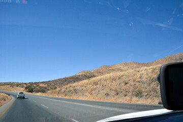 View from a car on an asphalt road in the desert in perspective with a car driving ahead