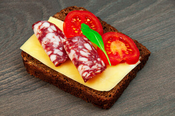 sandwich with sausage, cheese and tomato on a dark wooden background. a simple sandwich with cheese, sausage and greens	