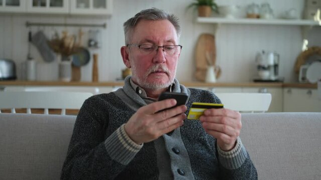 Senior man shopping online holding smartphone paying with credit card. Old grandfather buying on Internet enter credit card details. Online shopping delivery service Older generation modern tech usage