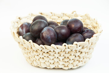 round blue plums in a basket on a white background. ripe sweet plums on a light texture	
