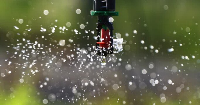 Super slow motion close up of automatic agricultural irrigation system is spraying water with splashing crystal clear pure water drops for watering crops and plants on field or garden at 1000 fps.