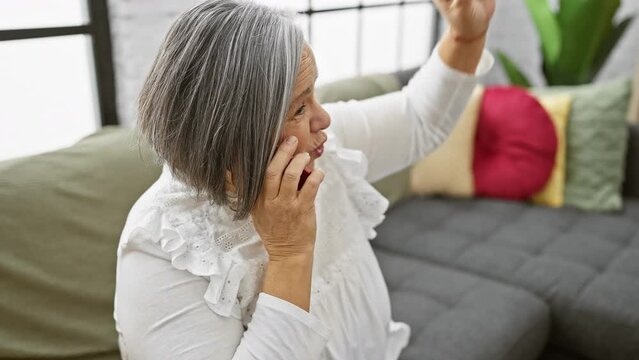 Mature woman talking on smartphone at home, showing comfort, communication, and casual lifestyle.
