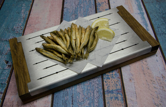 Fried seafood. Top view of fried whitebait, also known as cornalitos with lemon in a metal board with a rustic wooden background. 