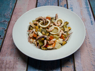 Delicious seafood salad. Top view of a salad made with shrimps, prawns, mussels, squid and vegetable pickles in a white bowl with a rustic wooden background.