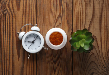 Fish oil capsules and alarm clock on a wooden table.