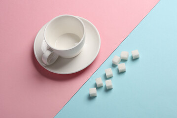 Obraz na płótnie Canvas Ceramic cup with sugar cubes on blue pink background