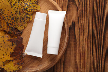 White cream tubes on a wooden plate with autumn leaves. Beauty mockup
