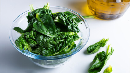 Fresh spinach leaves in a glass bowl with oil on white background.