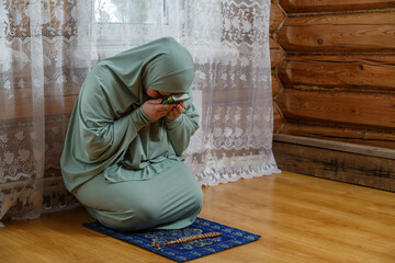 A Muslim woman in a light dress for prayer performs prayer while sitting on a mat and bowing