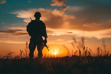 Fototapeta premium A Silhouette of a soldier stands in a field at sunset, holding his rifle. 