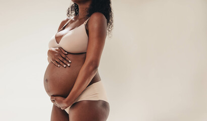 Pregnant black woman hugging her belly while wearing maternity lingerie