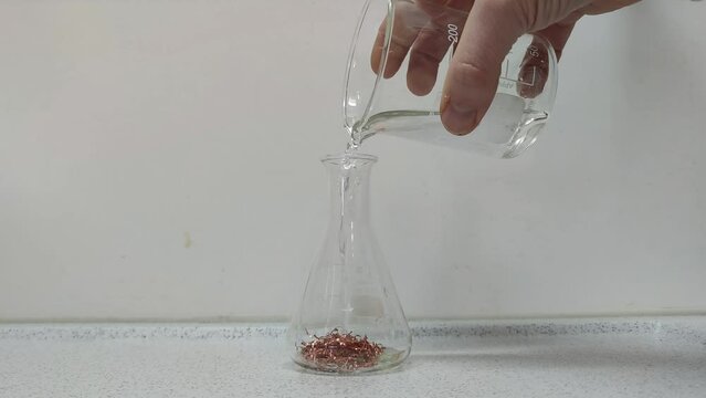 Chemical experiment in which Nitric acid (HNO3) is placed in an Erlenmeyer flask with copper chips, causing a violent chemical reaction. Example of a redox reaction in chemistry.