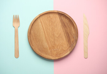 Wooden plate with fork and knife on a blue and pink background. Eco concept