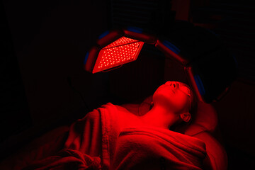 Relaxed female client having red LED light facial photodynamic therapy treatment in beauty salon....
