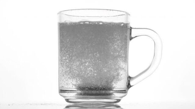 Effervescent tablet dissolve with bubbles in a glass of water, white background