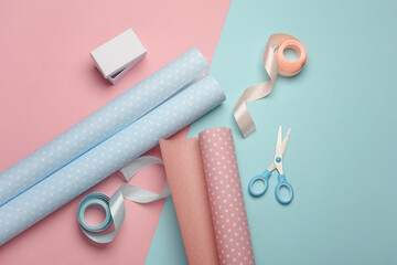 White box with satin ribbons and scissors, rolls of wrapping paper on pastel background. Holiday...