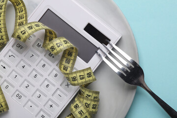 Plate with calculator, measure tape and fork on blue background. Reset evening, count calories