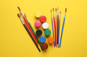 Jars of gouache paint with brushes on a yellow background
